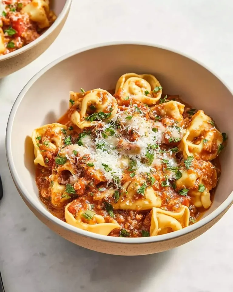 A close-up of a rustic bowl filled with delicious Crockpot Cheesy Tortellini, generously coated in a rich red sauce, grated Parmesan cheese, and fresh parsley.