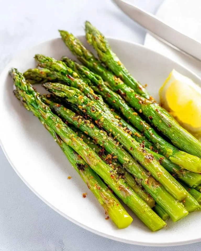 A white plate holds perfectly grilled asparagus spears seasoned with spices, accompanied by a fresh lemon wedge.
