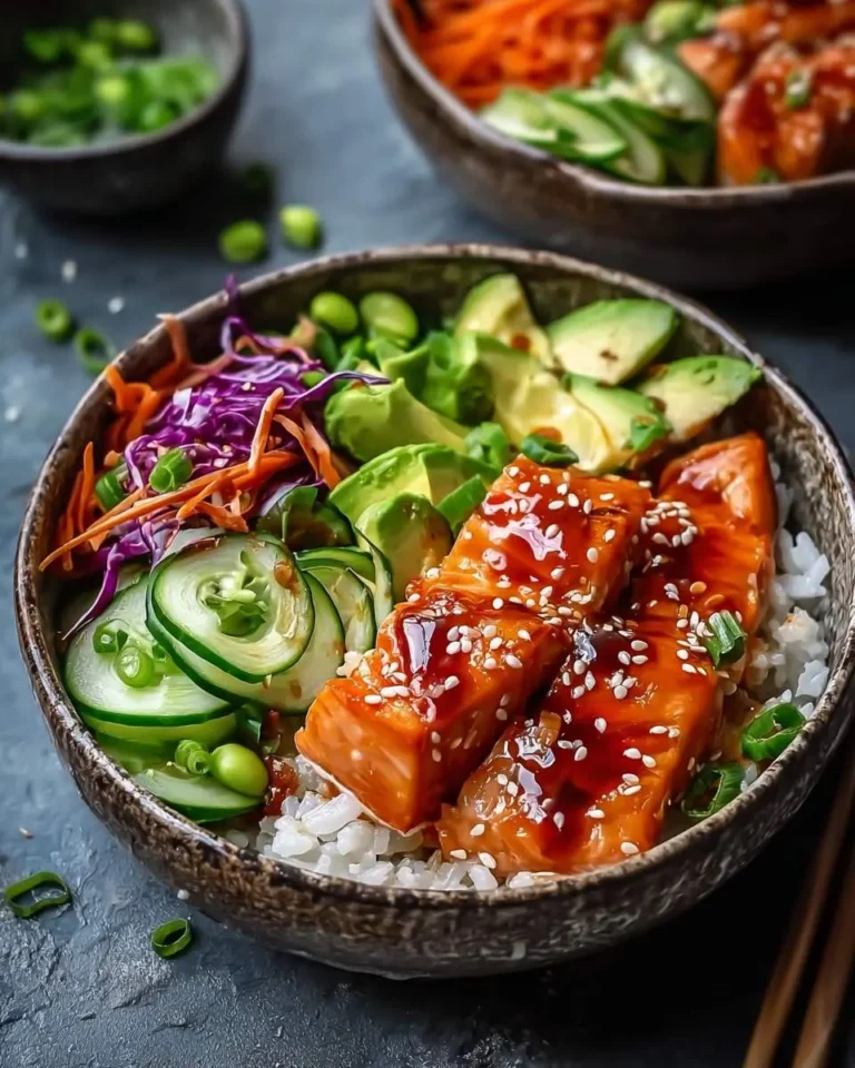 A close-up of vibrant Honey Sriracha Salmon Bowls featuring glazed salmon fillets, white rice, avocado, cucumber, red cabbage, carrots, edamame, and green onions.