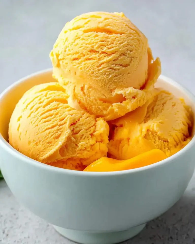 A light blue bowl filled with multiple scoops of vibrant orange mango ice cream, with some melted sauce at the bottom.