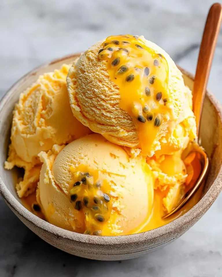 Close-up of a rustic bowl filled with golden Mango Passionfruit Ice Cream scoops, generously drizzled with fresh passion fruit pulp and seeds.
