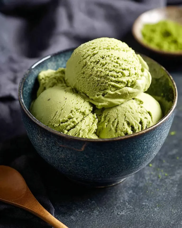 A rustic blue bowl filled with scoops of vibrant green matcha ice cream, possibly matcha banana ice cream, with a wooden spoon nearby.