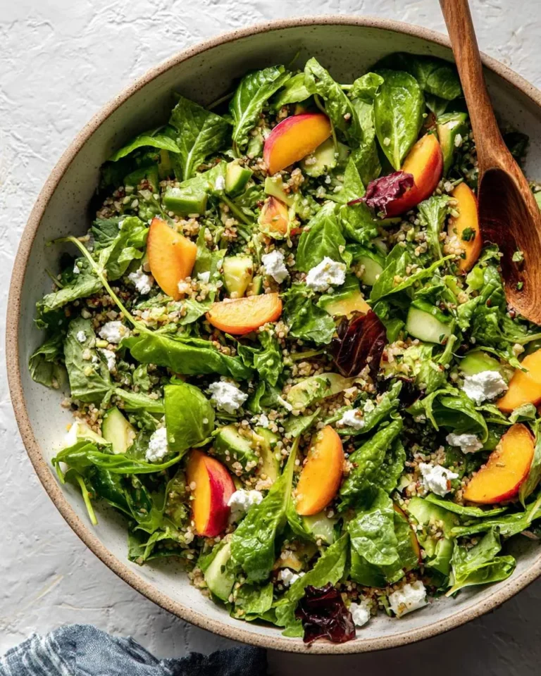 A vibrant Peach and Goat Cheese Salad with mixed greens, quinoa, and cucumber in a rustic ceramic bowl, ready to be served.