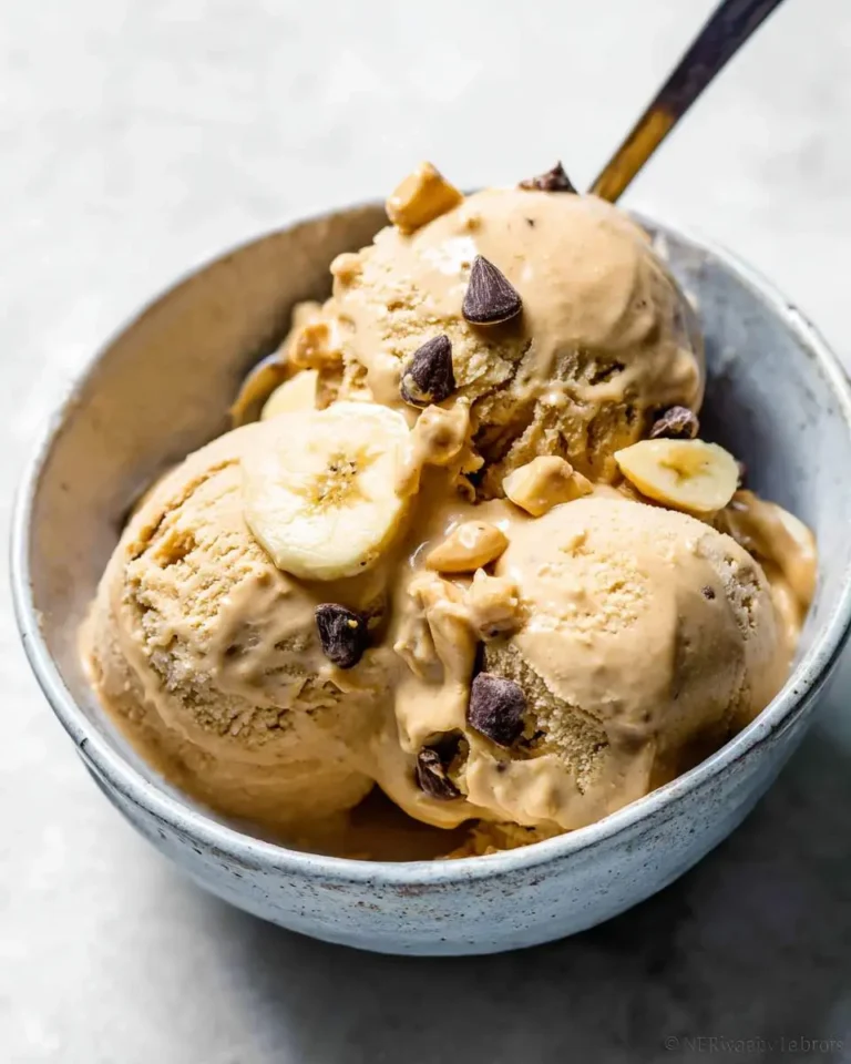 A rustic bowl filled with three scoops of creamy peanut butter banana ice cream, topped with chocolate chips, banana slices, and chopped nuts.