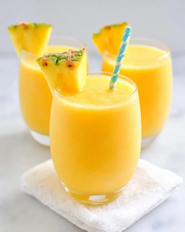 Three vibrant yellow Pineapple Orange Smoothies, two garnished with fresh pineapple wedges, and one with a blue and white straw.