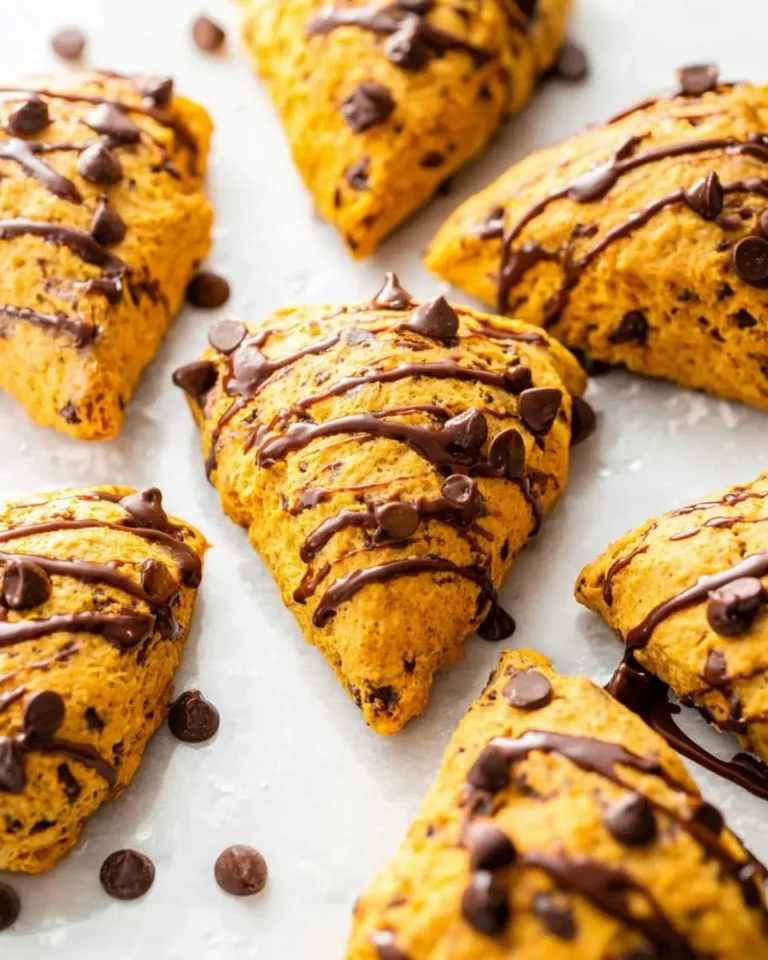 Close-up of several triangular pumpkin chocolate chip scones drizzled with dark chocolate and scattered with chocolate chips on a white surface.