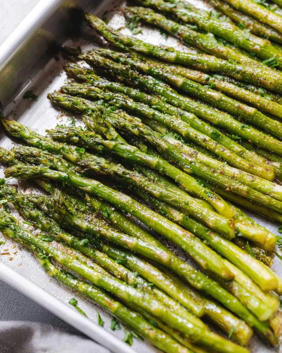 A close-up view of vibrant green roasted asparagus spears, seasoned and perfectly cooked in a metal baking pan.