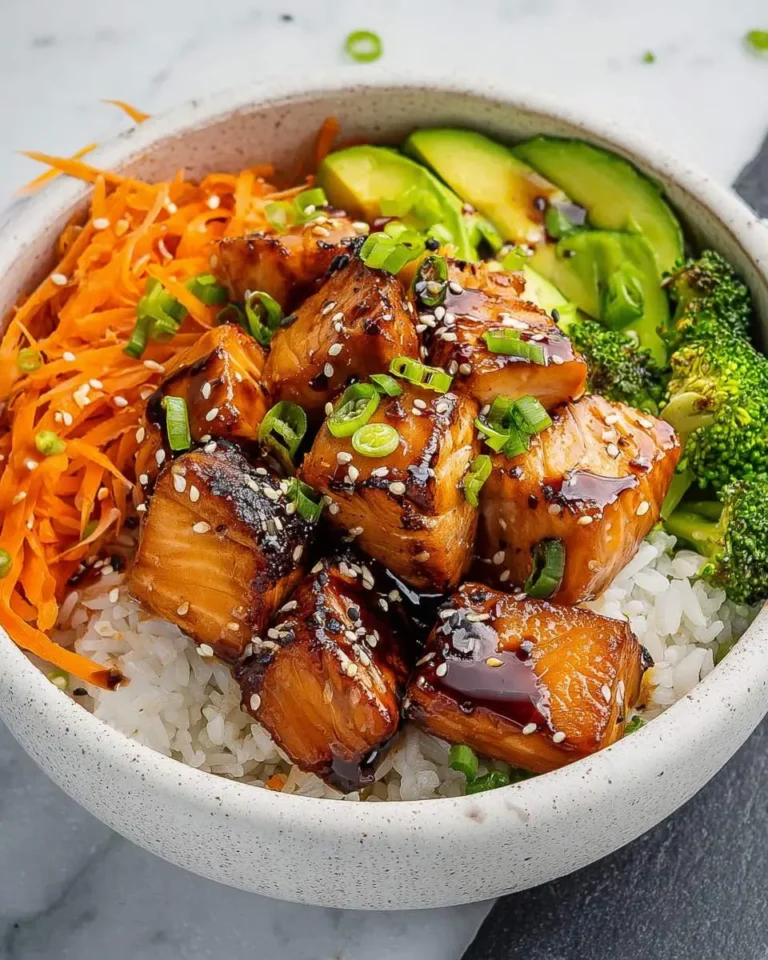 A delicious Salmon Teriyaki Bowl with glazed salmon, white rice, shredded carrots, avocado, and broccoli, topped with sesame seeds.