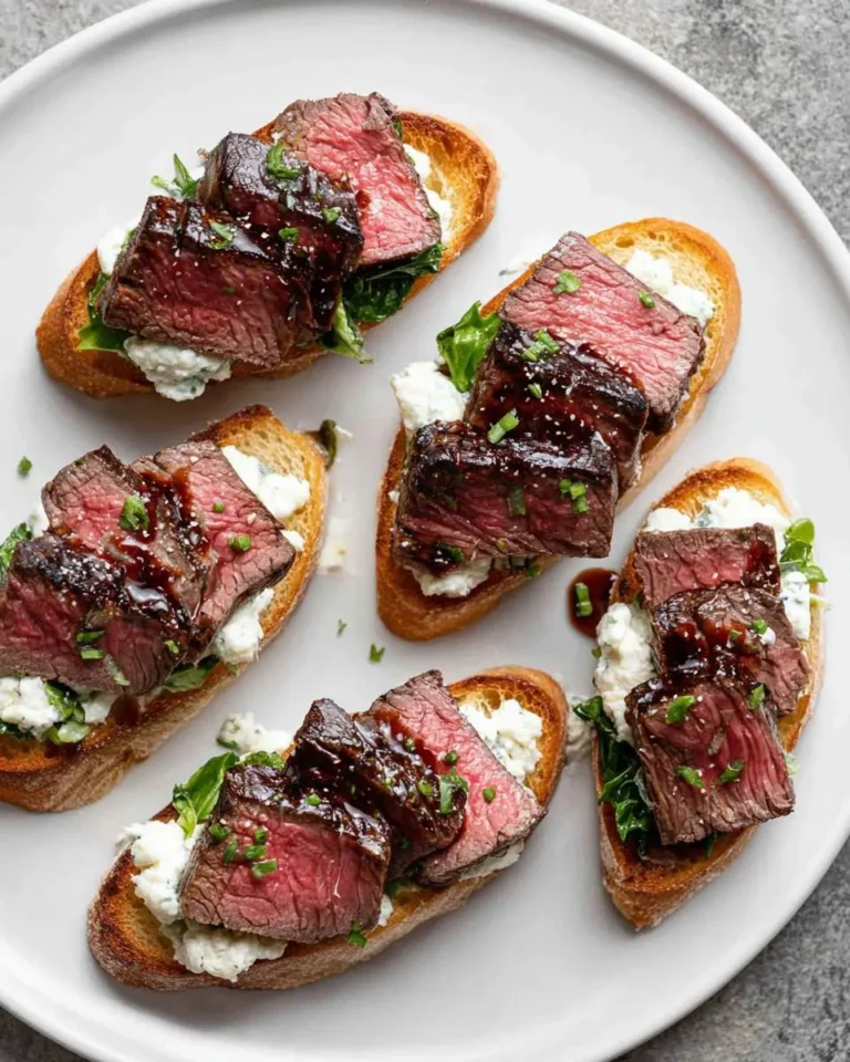 Close-up of several gourmet steak crostini appetizers featuring perfectly cooked medium-rare beef slices, creamy cheese, and a savory glaze on a white plate.