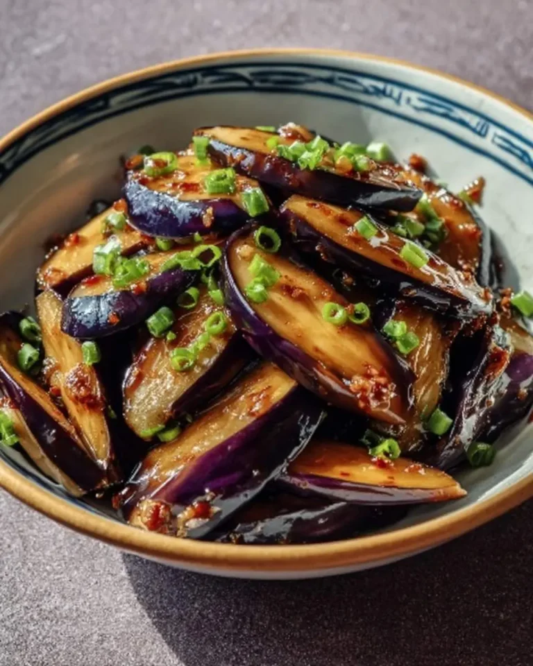 A close-up of beautifully prepared Aubergines sautées à l'ail, garnished with chopped green onions in a decorative bowl.