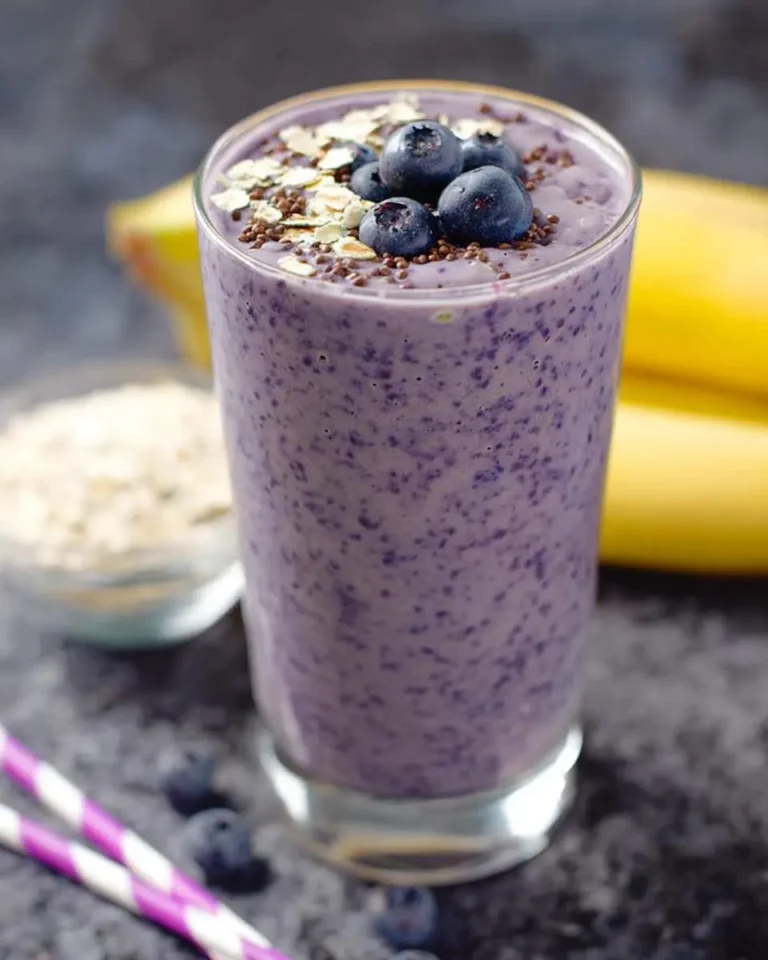 A refreshing Banana Blueberry Smoothie in a glass, garnished with fresh blueberries, oats, and sprinkles, with bananas and oats in the background.