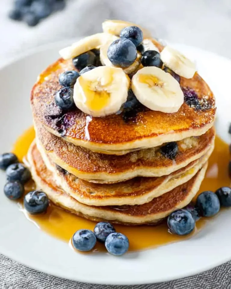 A delicious stack of golden Blueberry Banana Pancakes topped with fresh blueberries, banana slices, and maple syrup.