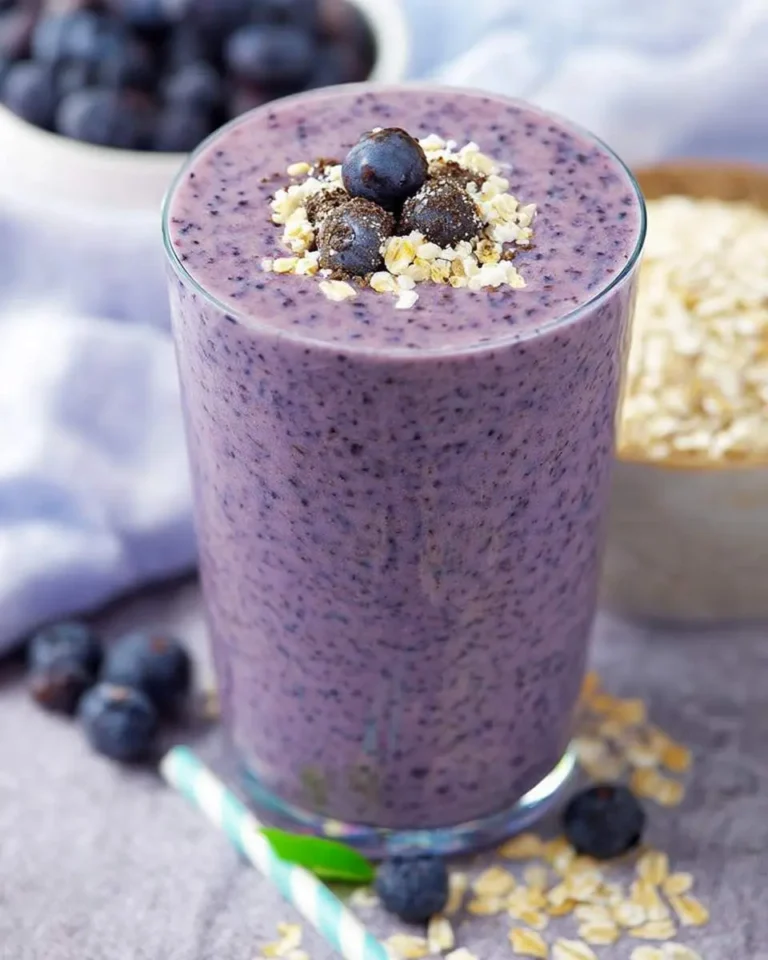 A vibrant purple Blueberry Oatmeal Smoothie in a glass, topped with fresh blueberries, crunchy oats, and cookie crumbs.