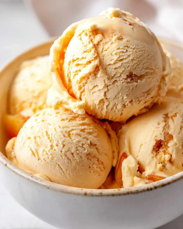 A bowl filled with delicious scoops of creamy brown butter peach ice cream, featuring visible peach pieces.