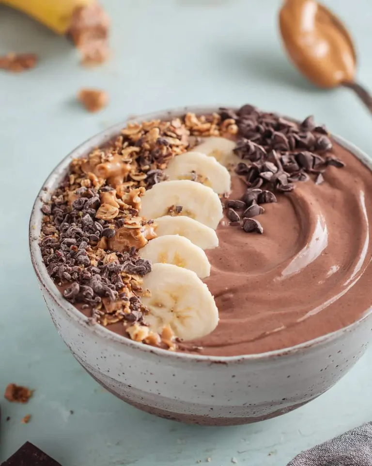 A close-up shot of a creamy Chocolate Peanut Butter Smoothie Bowl topped with banana slices, granola, and chocolate chips.