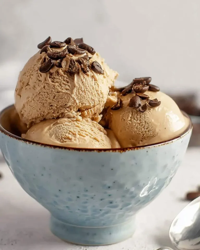 Three scoops of creamy coffee ice cream topped with whole and crushed coffee beans in a speckled blue bowl.