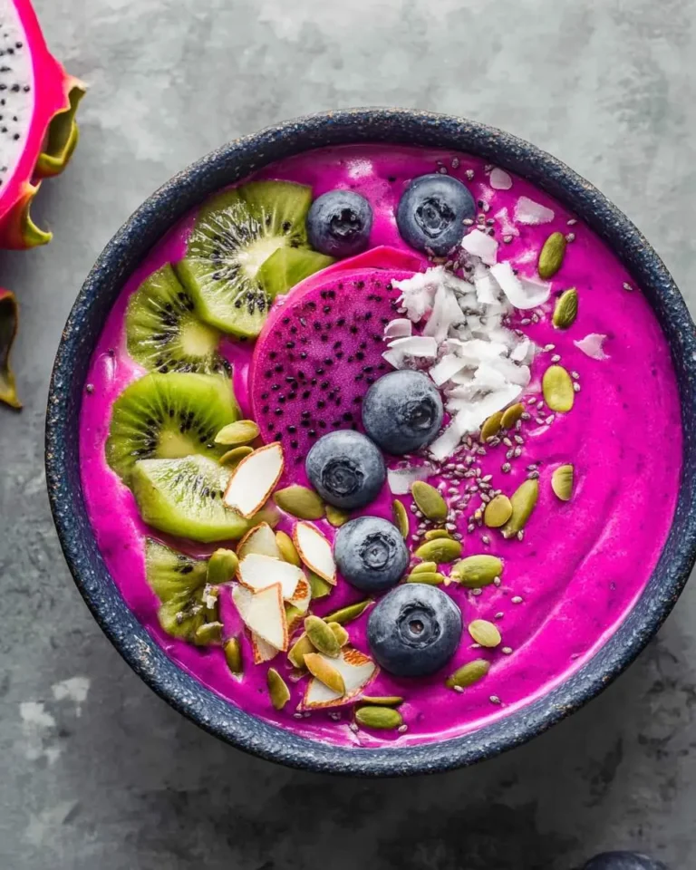 A vibrant pink Dragon fruit smoothie bowl topped with fresh kiwi slices, blueberries, dragon fruit, coconut, pumpkin seeds, and almonds.