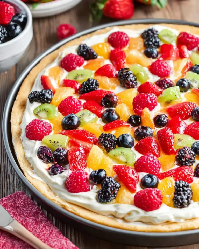A vibrant, round fruit pizza topped with a creamy white frosting and a colorful array of fresh fruits like raspberries, blueberries, kiwi, strawberries, and orange segments, presented in a dark pan on a wooden table.