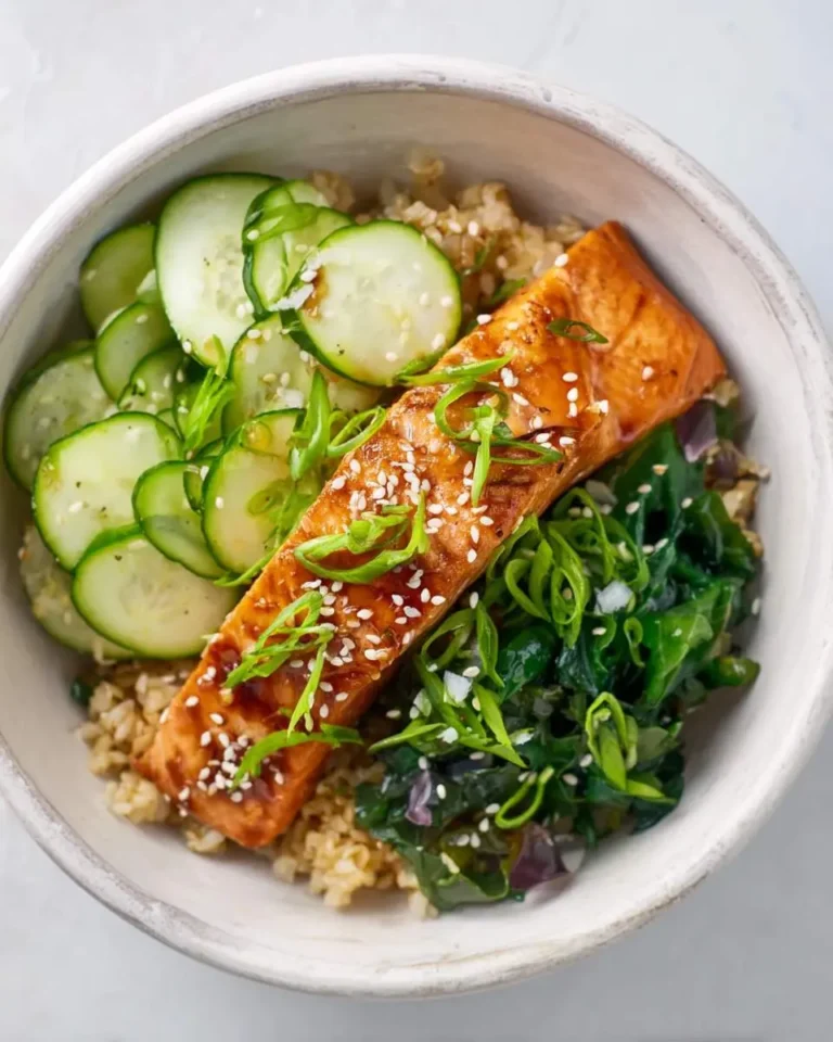 A beautiful Miso Glazed Salmon Bowl with brown rice, sliced cucumbers, and green seaweed salad, garnished with sesame seeds and scallions.