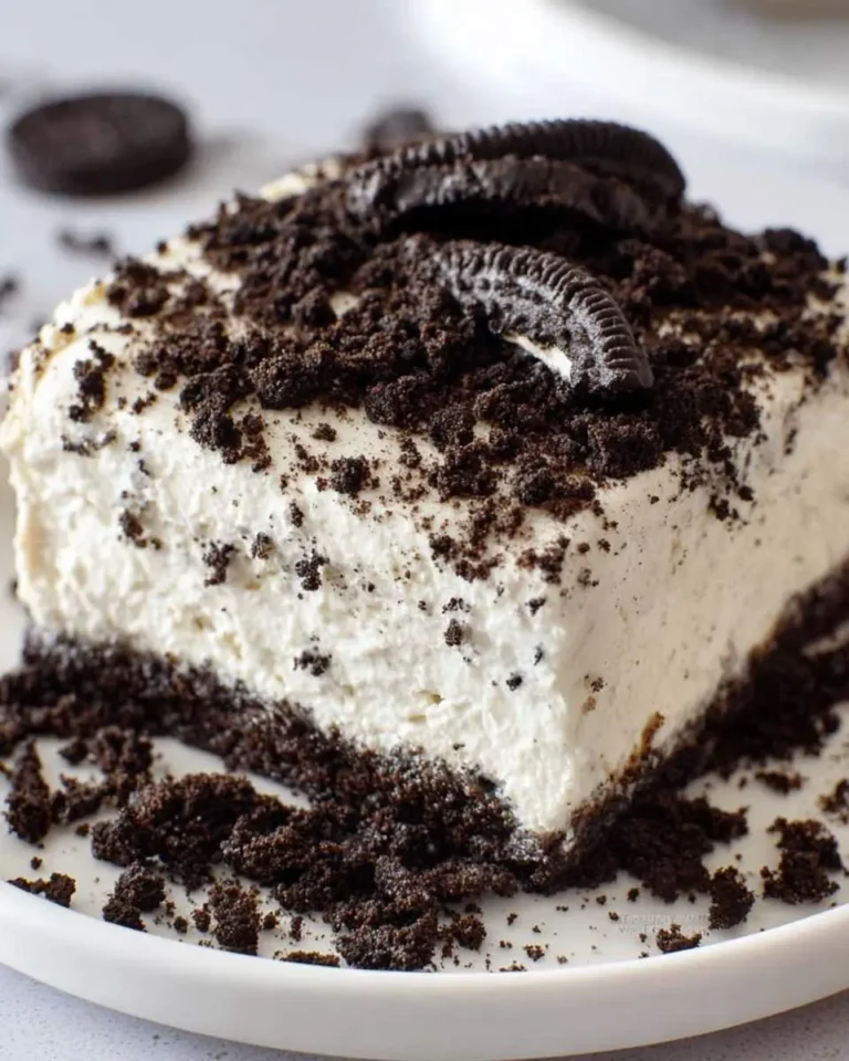 A delicious slice of Oreo Dirt Cake, featuring creamy white filling, crushed Oreo cookies, and mini Oreo cookie garnishes on a white plate.