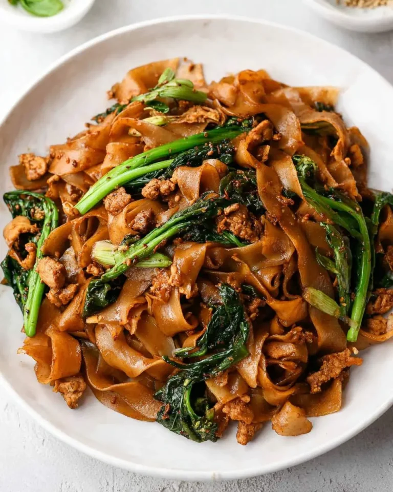 A close-up shot of a savory plate of Pad See Ew, featuring wide rice noodles, tender chicken, and vibrant Chinese broccoli.