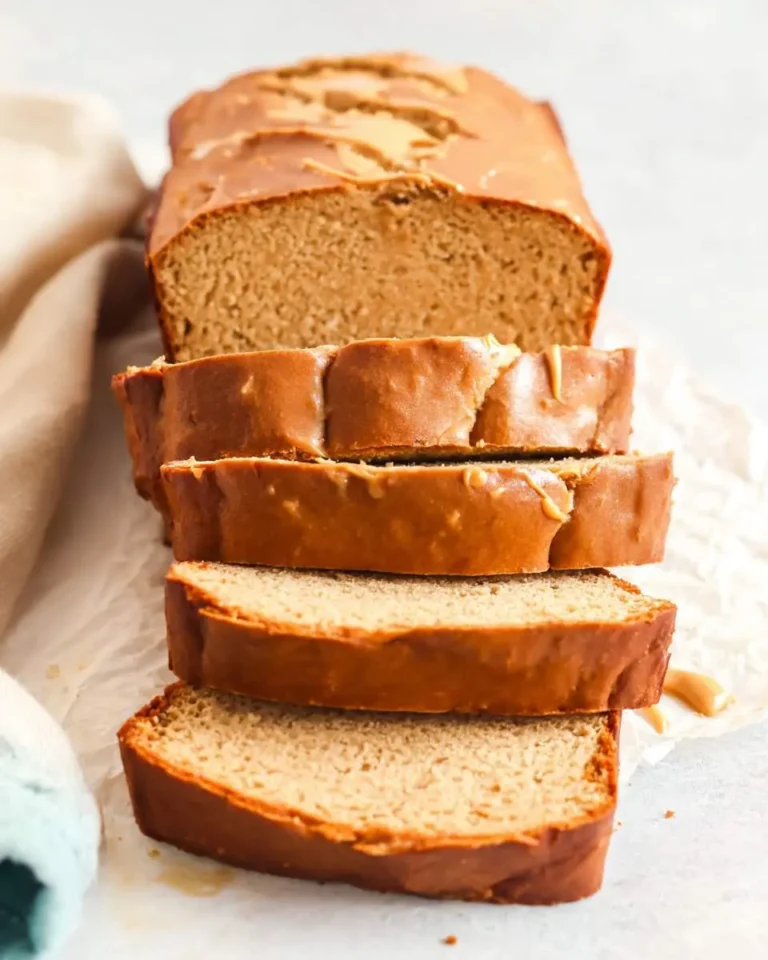 A delicious loaf of sliced Peanut Butter Bread with a light glaze on white parchment paper, ready to be served.