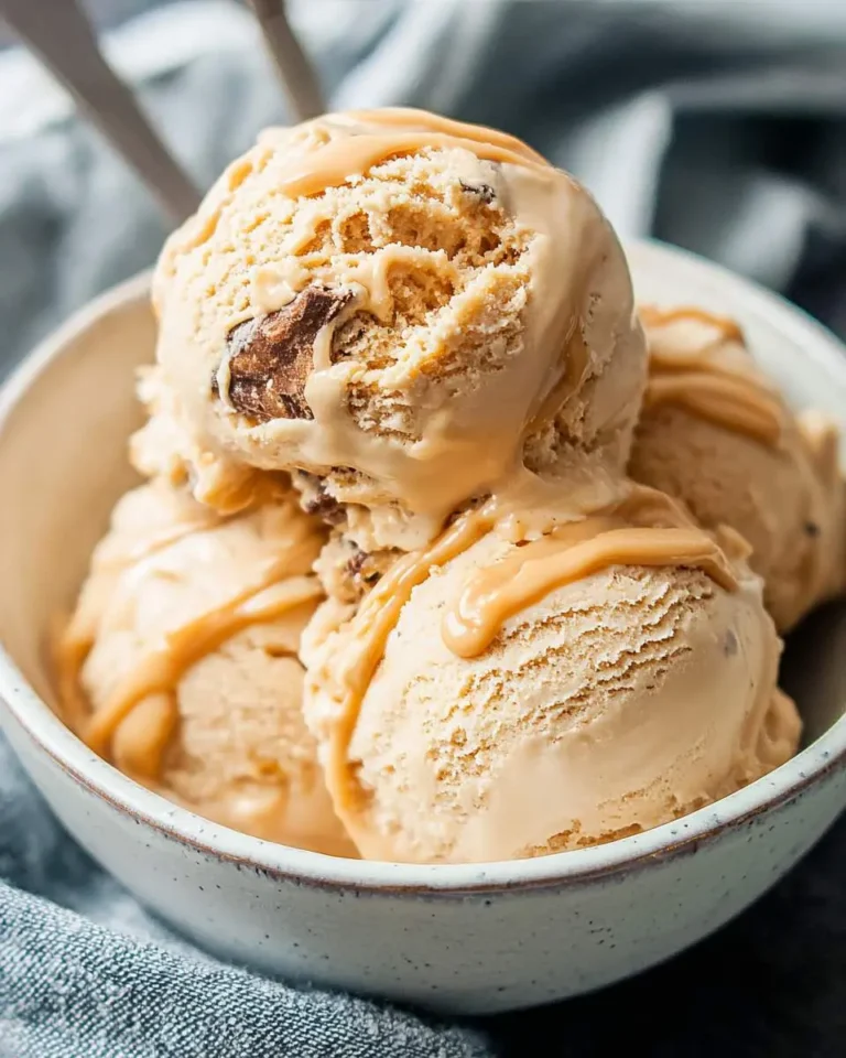 A bowl of delicious peanut butter ice cream scoops topped with a creamy drizzle and visible chocolate or peanut butter chunks.