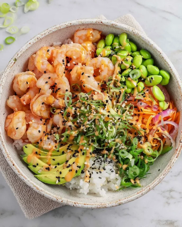 A vibrant Shrimp Poke Bowl with rice, avocado, edamame, carrots, and a delicious sauce, sprinkled with sesame seeds.