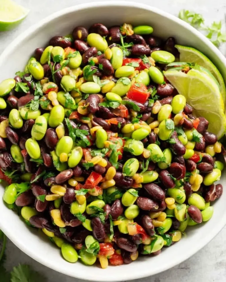 A white bowl filled with colorful Black Bean Edamame Salad garnished with lime wedges and fresh cilantro.