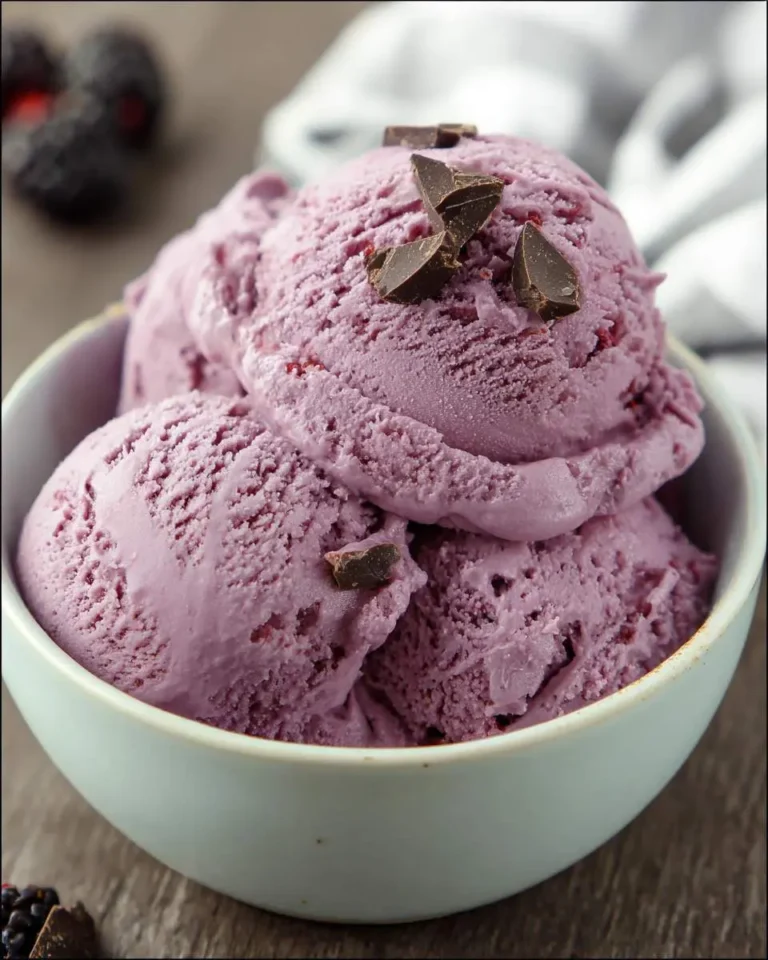 Three scoops of creamy Blackberry Ice Cream topped with chocolate chunks in a white bowl.