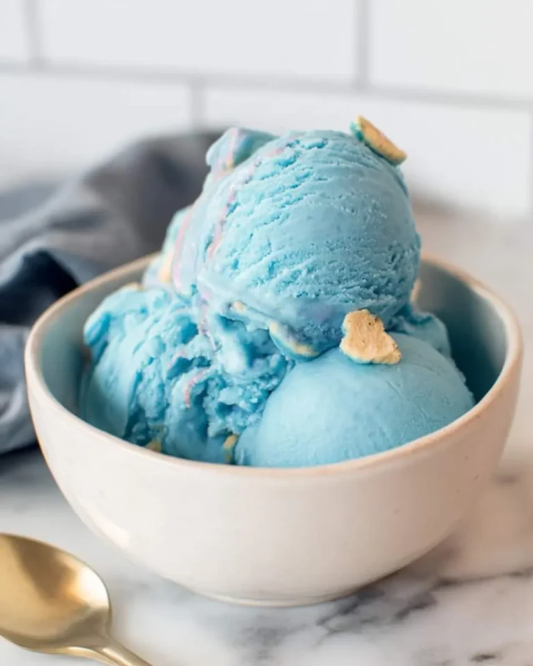 Three scoops of vibrant blue moon ice cream in a white bowl with cookie pieces visible.