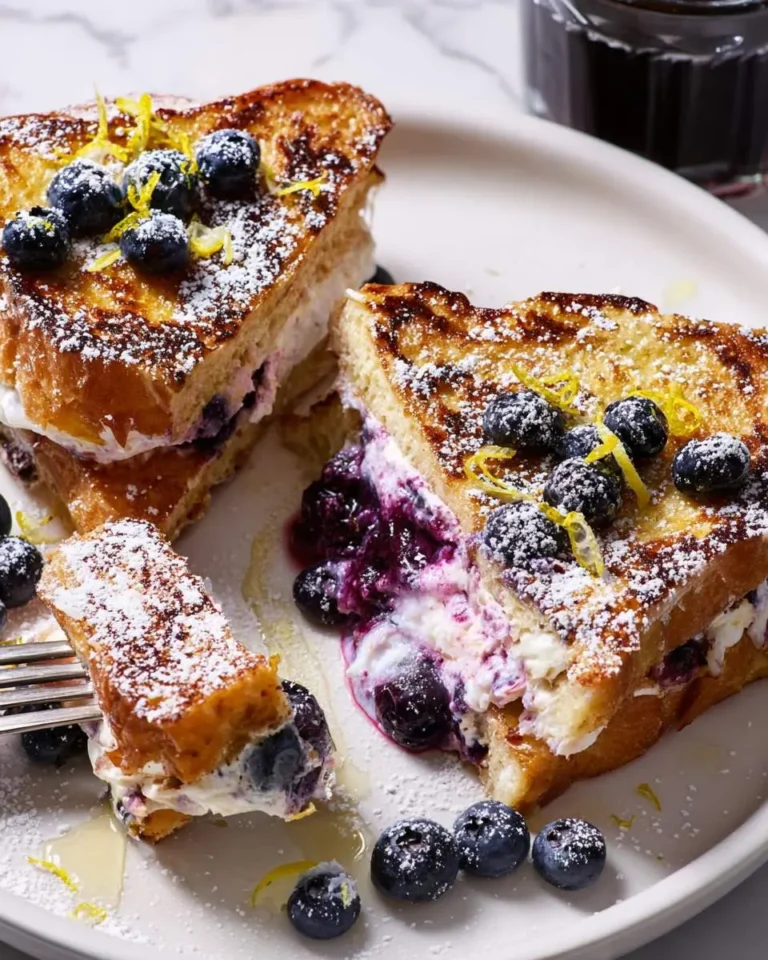Blueberry-Lemon Ricotta Stuffed French Toast topped with fresh blueberries, lemon zest, and powdered sugar on a white plate.