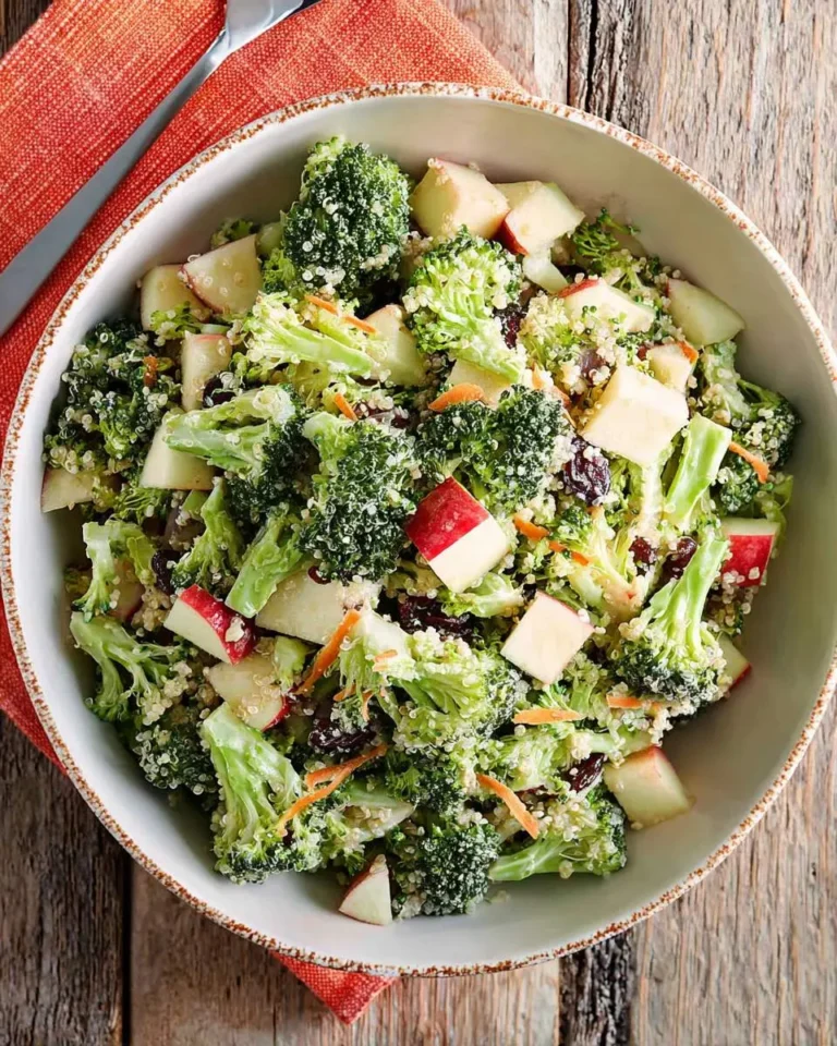 Fresh Broccoli Apple Quinoa Salad served in a white bowl with diced apples, dried cranberries, and shredded carrots on a rustic wooden table.