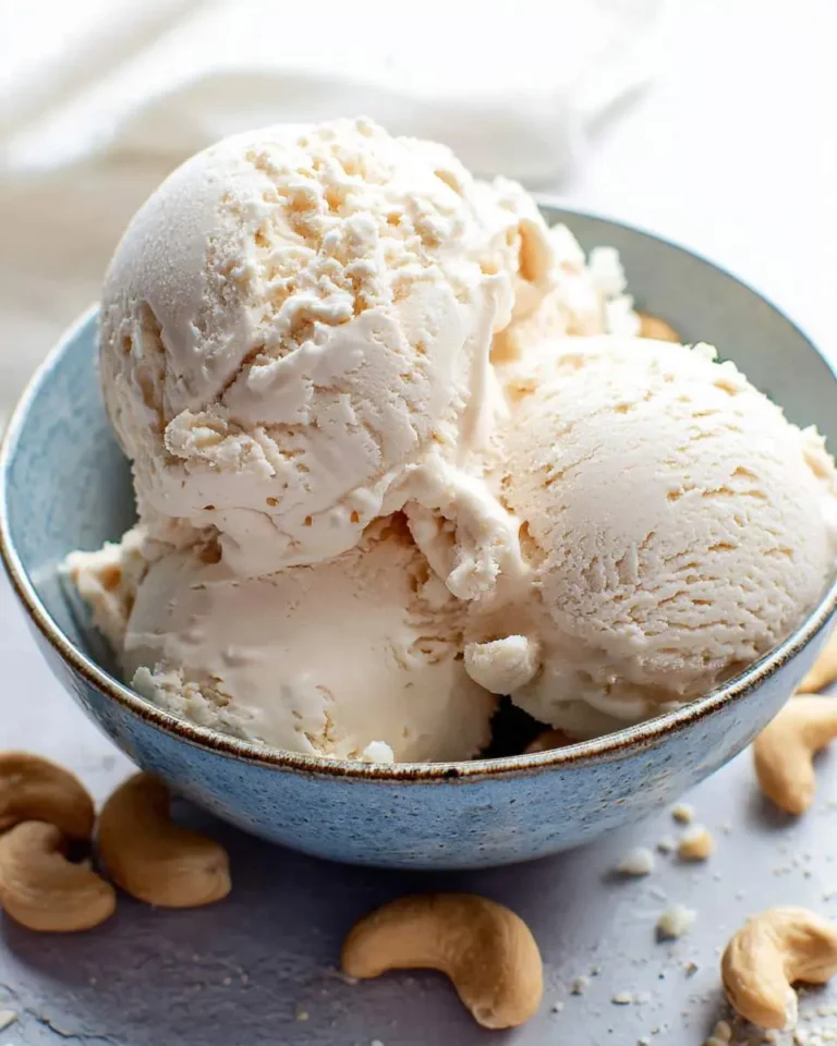 Three scoops of creamy cashew ice cream served in a blue ceramic bowl with cashews scattered around.
