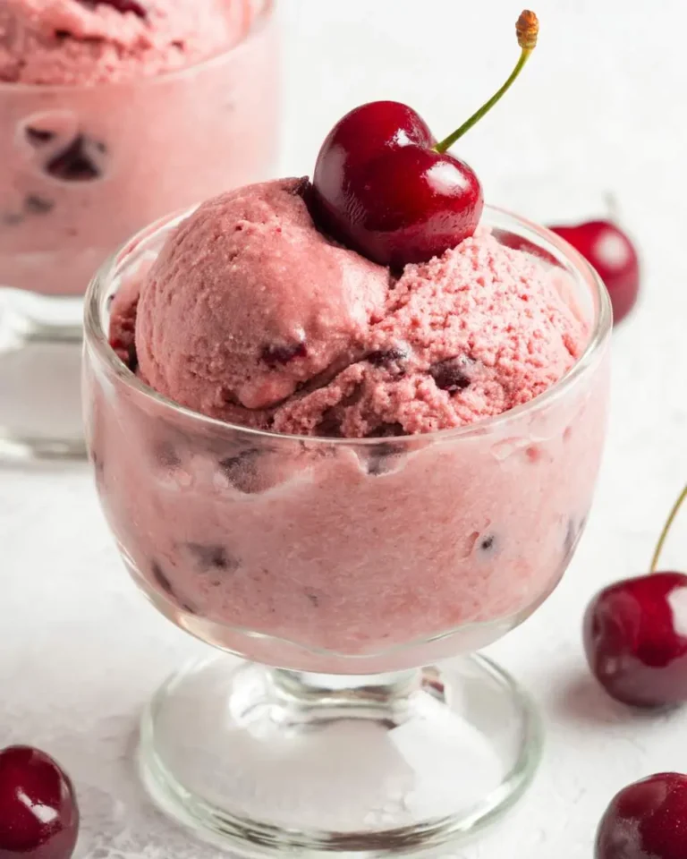 Cherry Garcia nice cream served in a glass dessert bowl, topped with a fresh cherry.