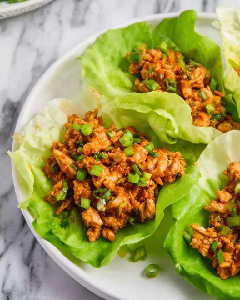 Three chicken lettuce wraps on a white plate, filled with seasoned ground chicken and topped with green onions.