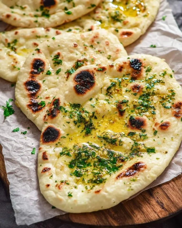 Freshly made Garlic Naan Bread topped with melted butter and chopped cilantro, displayed on parchment paper.