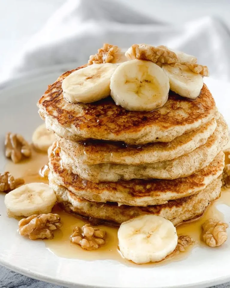 Stack of golden gluten-free banana pancakes topped with fresh banana slices, walnuts, and maple syrup on a white plate.