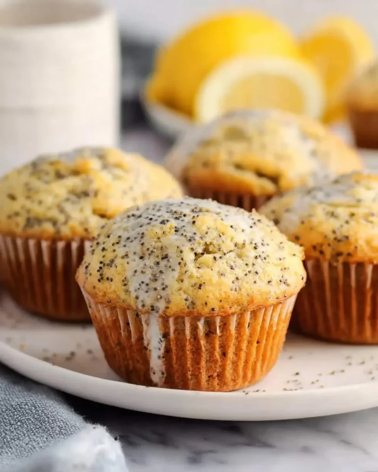 Freshly baked lemon poppy seed muffins with glaze on a white plate, with lemons in the background.
