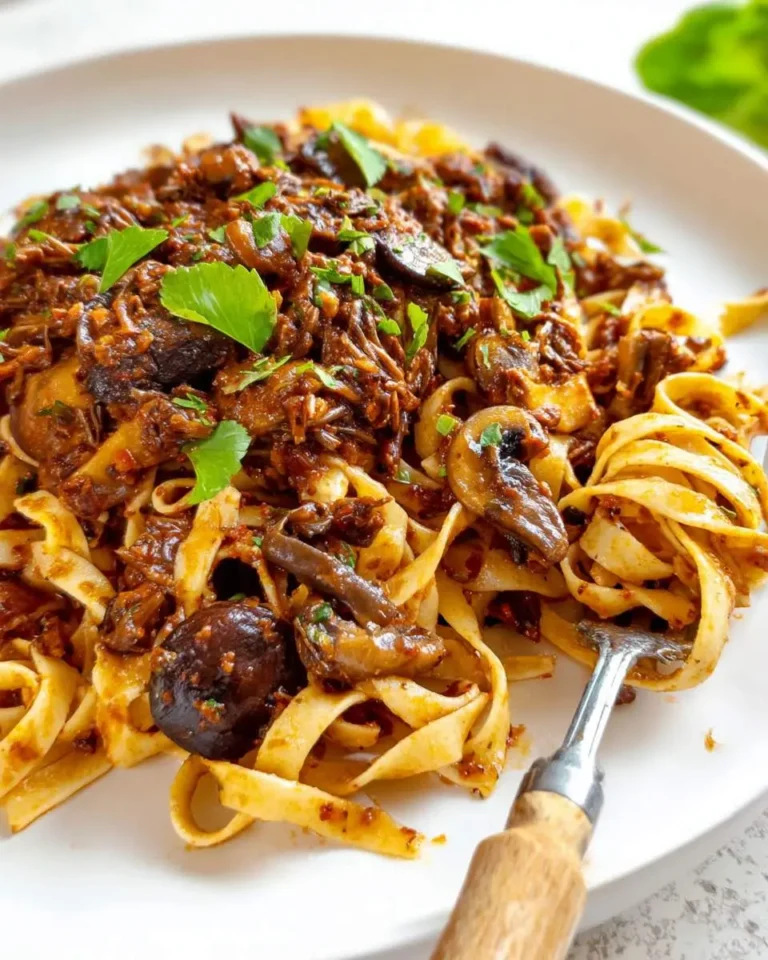 A plate of wide ribbon pasta topped with rich mushroom ragu and fresh herbs, with a fork twirled in the noodles.