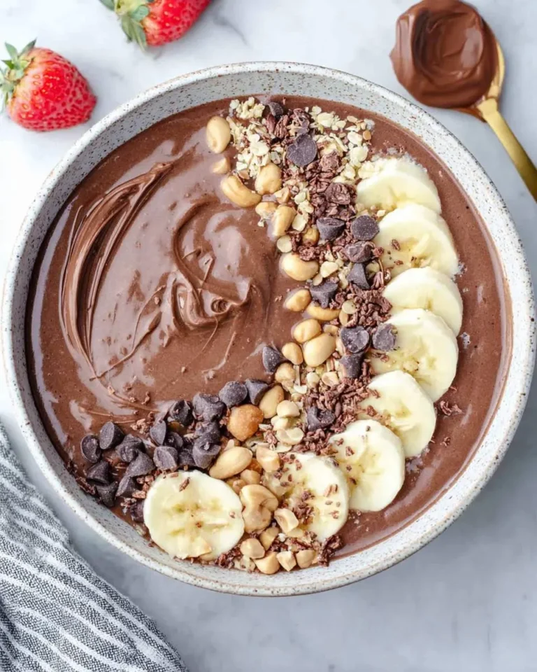 A creamy Nutella Smoothie Bowl topped with banana slices, chocolate chips, peanuts, and granola in a speckled bowl.