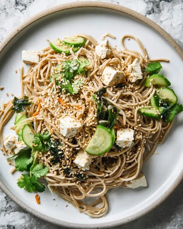 A plate of Sesame Soba Noodles topped with tofu cubes, cucumber slices, fresh cilantro, and toasted sesame seeds.