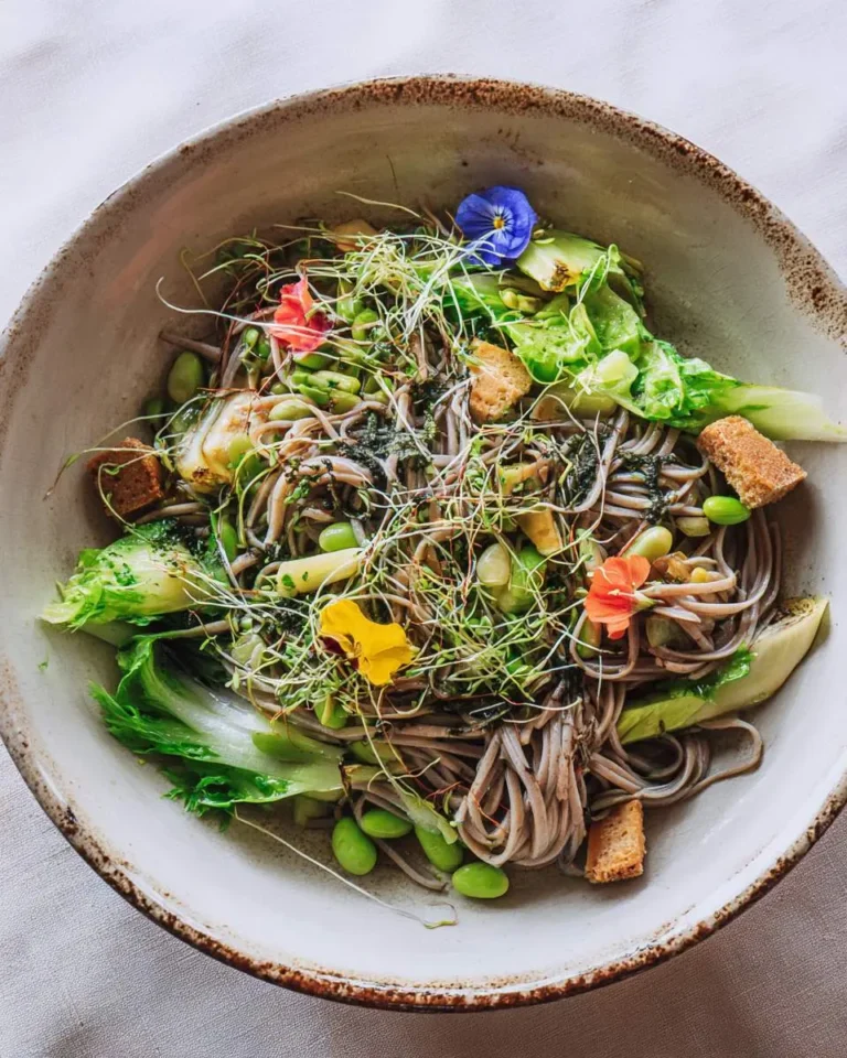Fresh soba noodle salad with edamame, bok choy, microgreens, and edible flowers in a ceramic bowl.