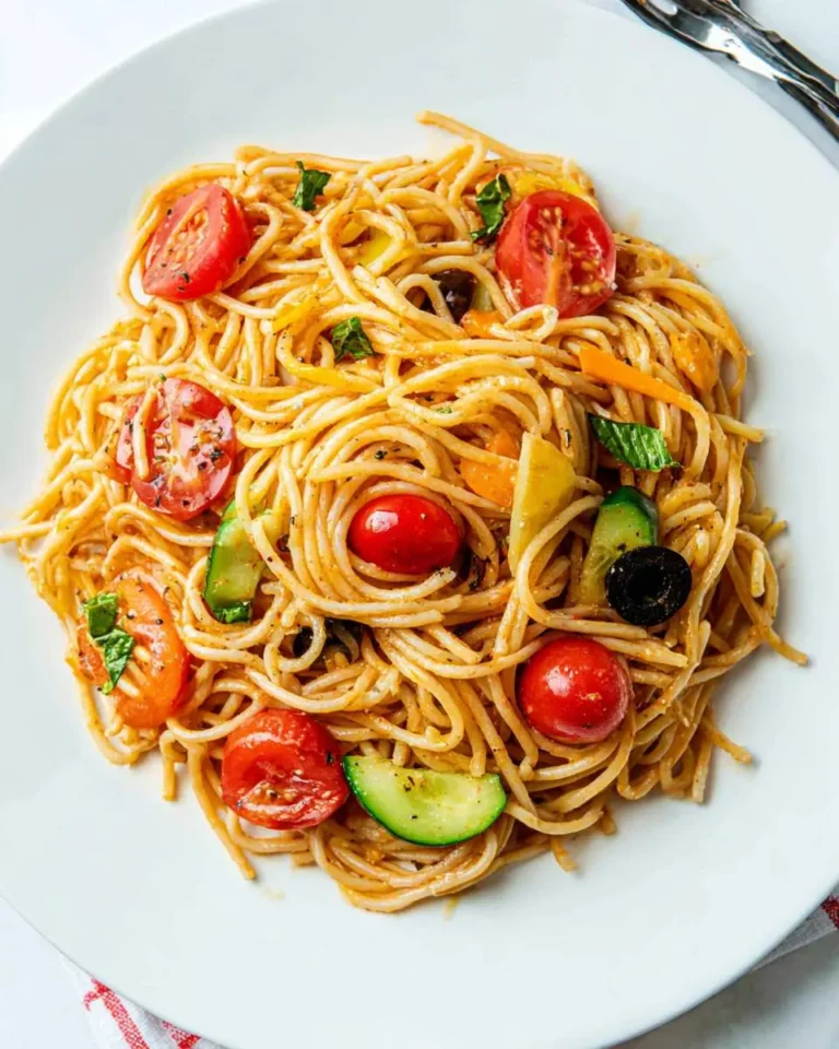 A plate of colorful spaghetti salad with cherry tomatoes, cucumbers, olives, and fresh basil on a white dish.