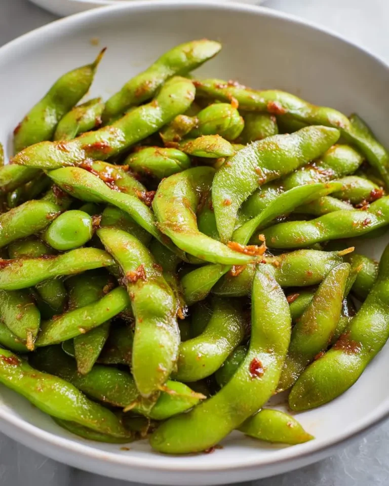 A white bowl filled with Spicy Garlic Chili Edamame, glistening with red chili flakes and seasoning.