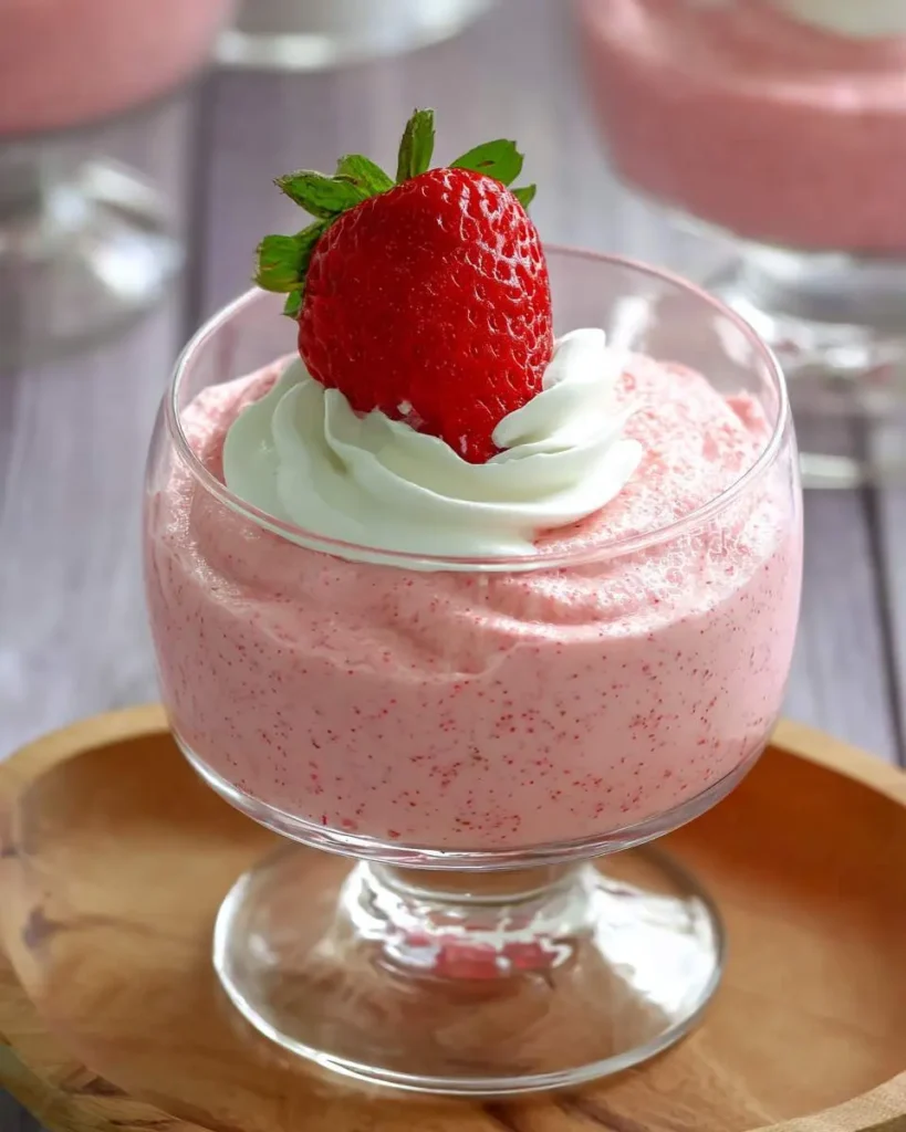 A glass dessert cup filled with creamy strawberry mousse topped with whipped cream and a fresh strawberry.