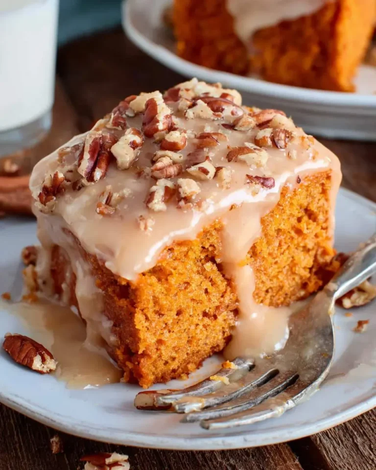 A slice of Sweet Potato Spice Cake topped with caramel glaze and chopped pecans on a white plate with a fork.