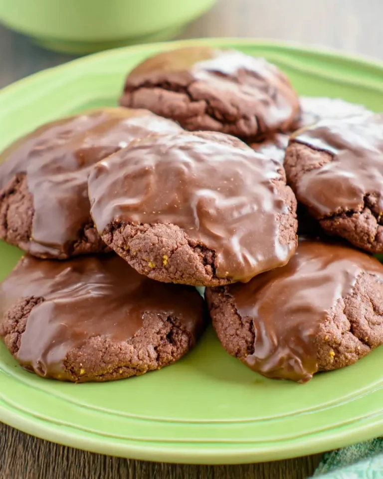 Stack of Texas Sheet Cake Cookies with glossy chocolate frosting on a green plate.