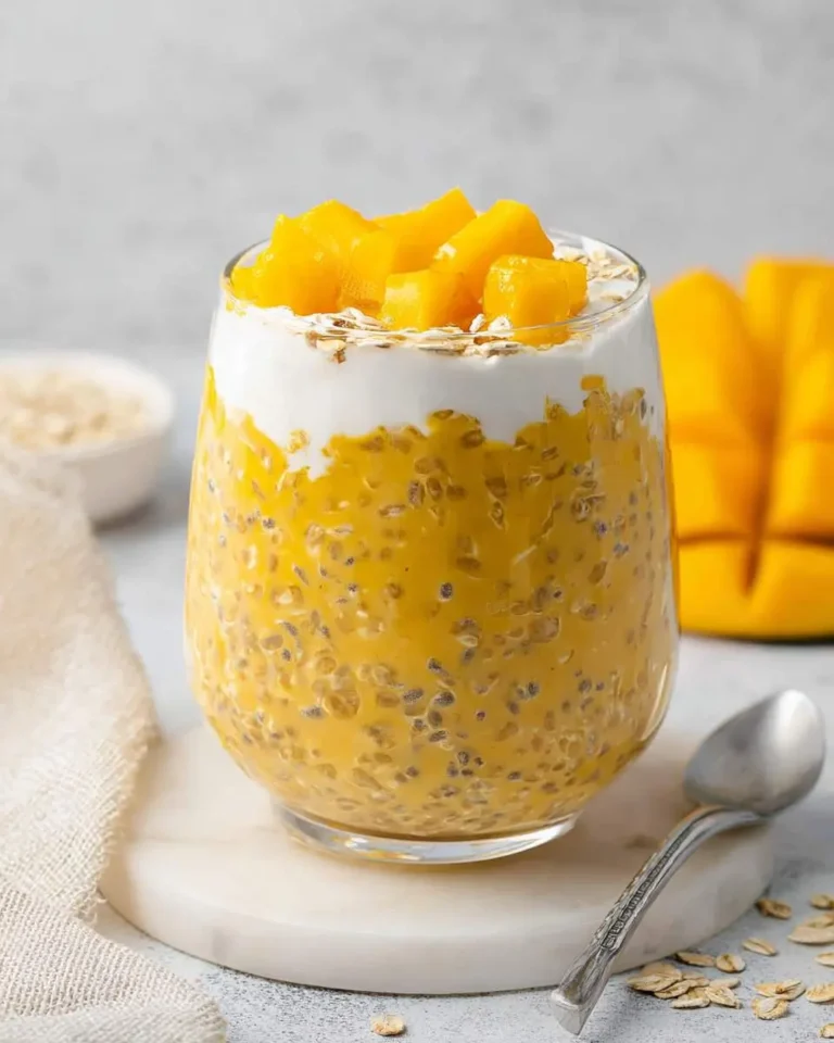 Tropical Mango Overnight Oats in a glass jar topped with fresh mango chunks, yogurt, and oats on a marble coaster.