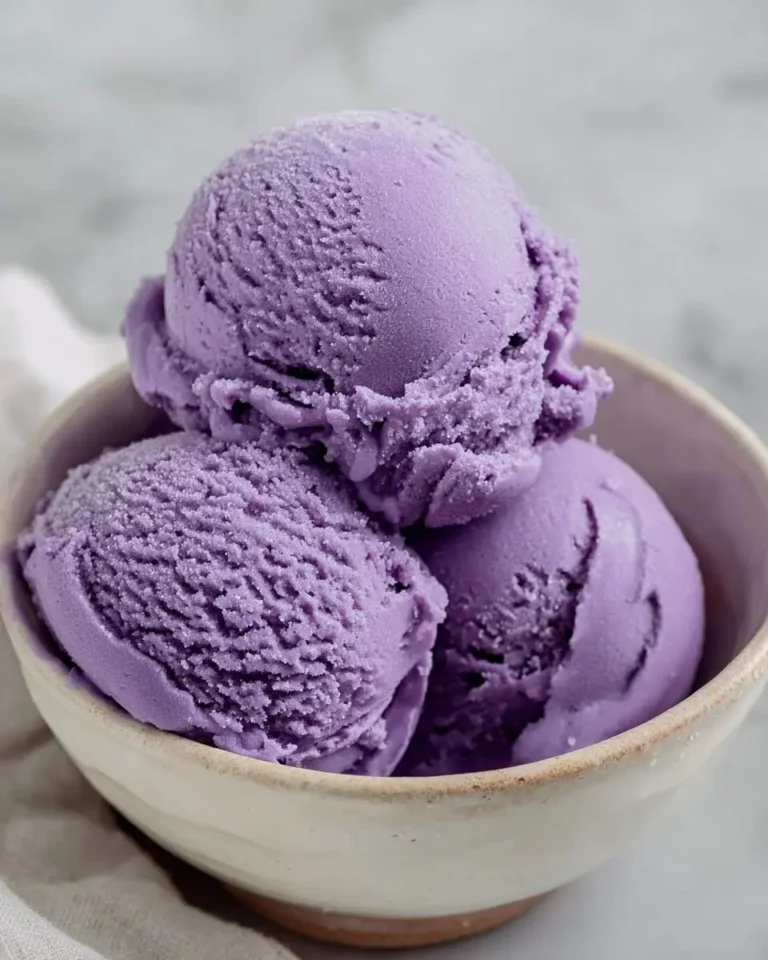 Three scoops of creamy purple ube ice cream recipe served in a rustic ceramic bowl on a marble surface.